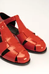 Sandalia roja de cuero vacuno con diseño de tiras entrecruzadas y hebilla lateral. Tiene suela de cuero artesanal y taco bajo.