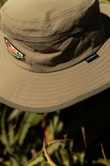 Sombrero tipo pescador color beige con ala ancha, borde reforzado, correa ajustable y parche frontal con el logo de Denali.