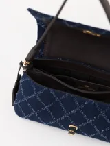 Bandolera confeccionada en denim azul con diseño acolchado en forma de rombos. Tiene correa de cuero marrón, cierre con torniquete metálico dorado y tag colgante con aplique de hongo.