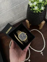 Reloj Casio Quartz dorado con caja cuadrada, dial negro y pulsera de eslabones.