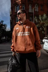 Buzo marrón con cierre medio, cuello alto y corte oversize. Estampado frontal con el número 19, un ancla con laureles y la frase "Refuse to Lose".