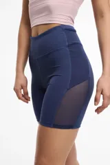 Calza deportiva corta color lila, de cintura alta, con bolsillos laterales y transparencias de microtul en los laterales.