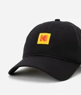 Gorra negra de sarga de algodón con visera curva, hebilla ajustable y logo de Kodak bordado en amarillo y rojo.