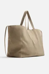 Bolso tipo shopper color topo, fabricado en piel con acabado serraje. Cuenta con dos asas de mano y un bolsillo pequeño con cierre mediante cremallera en su interior.