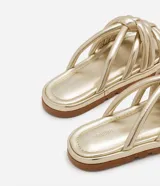 Sandalia plana de color negro con diseño de tiras tubulares acolchadas tipo puffer entrelazadas con nudos. Presenta puntera redonda, plantilla anatómica y suela de goma al tono.