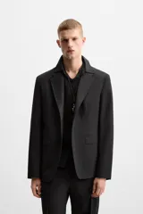 Blazer negro de lana con cuello de solapa de muesca, corte recto, manga larga con puños abotonados, bolsillos de vivo en el pecho y de solapa en la cadera, abertura en la parte posterior y cierre frontal con botones. Colección Origins.