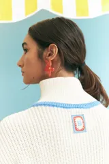 Sweater de punto grueso color crudo, con cuello alto con cierre de cremallera y rayas horizontales en azul, amarillo y rojo.
