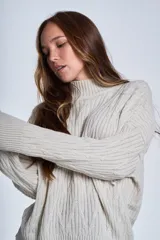 Sweater color crema de punto trenzado, con cuello alto y mangas largas.