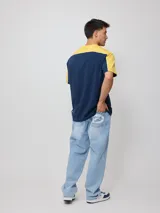Remera de hombre azul marino con mangas y cuello amarillo, y logo de la marca Rusty estampado en el pecho.