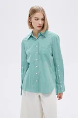 Camisa a rayas verticales verdes y blancas, de corte holgado, manga larga con puños abotonados, cuello clásico y bolsillo de parche en el pecho.