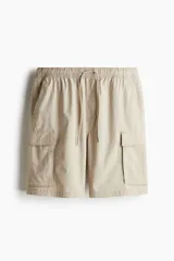 Short color beige de tejido grueso de algodón, con corte estándar, cintura elástica con cordón ajustable, bolsillos al bies y bolsillos de solapa con cierre autoadherente en las piernas y atrás.