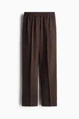 Pantalón marrón de corte holgado en sarga de mezcla de lyocell. Modelo de tiro alto con cintura fruncida, cierre decorativo y bolsillos laterales discretos. Piernas rectas con pliegues cosidos adelante y raya planchada atrás.