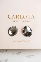 Aros metálicos plateados con forma ovalada y superficie ondulada. Fabricados en acero quirúrgico, resistentes al agua, hipoalergénicos y livianos.