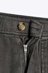 Pantalón gris oscuro de tiro alto con cintura elástica, bolsillos delanteros y falsos bolsillos con solapa en la espalda. Cierre frontal con cremallera y botón.
