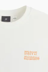 Remera blanca de algodón de corte holgado con estampado del artista Keith Haring en el pecho. Modelo de H&M con cuello redondo y mangas cortas.