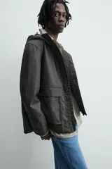 Parka relaxed fit color negro confeccionada en tejido de lino que repele el agua. Tiene cuello con capucha ajustable, mangas largas con puños abotonados, bolsillos frontales con solapa y cierre frontal con cremallera oculta por solapa con botones a presión.