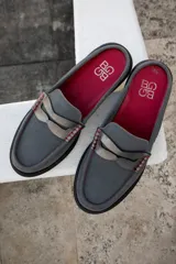 Mocasín mule de cuero gris con detalle de aplique plateado y costuras rojas. Interior color fucsia con logo estampado.