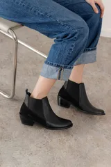 Botín negro de cuero con paneles laterales de gamuza y elástico en los tobillos. Tiene un pequeño taco cuadrado.