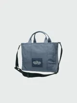 Bolso tote negro de lona con doble asa de mano y correa bandolera ajustable y extraíble. Estampado frontal con el texto "THE TOTE BAG MARC JACOBS" en color blanco.