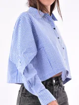 Camisa corta a la cintura, a rayas verticales azules y blancas, con cuello clásico y cierre frontal con botones negros.