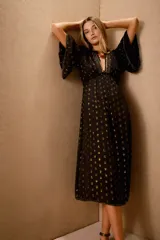Vestido largo negro con estampado de lunares dorados, mangas al codo y corte amplio con ajuste elástico en la cintura. Presenta bordados de lentejuelas y mostacillas en el escote y mangas.