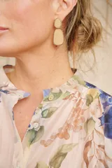 Aros colgantes con forma abstracta, color beige con textura tejida y borde dorado.