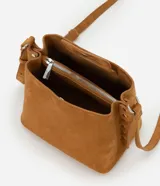 Cartera de gamuza color tostado, de tamaño mediano, con diseño transversal y asa larga ajustable. Cuenta con cierre superior de botón a presión, compartimento interno principal y detalles laterales con ojales metálicos.