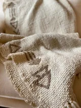 Manta de lana color crudo con bordados de flechas en color marrón.