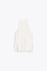 Top blanco sin mangas con cuello halter y volantes en los bordes. Cierre con botón oculto en la espalda.