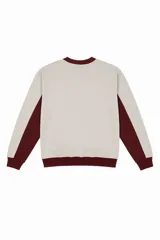 Buzo beige de corte oversize con cuello redondo y ribete burdeos en cuello, puños y cintura. Presenta paneles laterales burdeos con vivo blanco y logo Vernal bordado en el pecho.