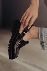 Zueco negro con textura croco, diseño tipo mocasín y tira regulable al talón.
