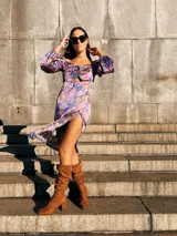 Vestido corto con estampado floral en tonos violeta, azul y amarillo. Tiene escote fruncido con cordones, mangas largas abullonadas y tajo lateral.