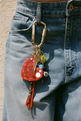 Llavero metálico con mosquetón dorado y charms colgantes desmontables: corazón rojo con espejo interior, llave, pelota de tenis, tiburón azul y bola de billar número 8.