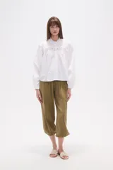 Camisa blanca de algodón con mangas largas abullonadas y cuello mao con volado. Presenta un canesú con detalles de encaje calado en el frente.