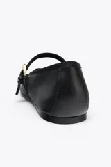 Zapato plano tipo bailarina color negro, confeccionado en piel, con tira sobre el empeine y hebilla metálica dorada ajustable. Tiene punta redonda y suela de 1.5 cm de altura.