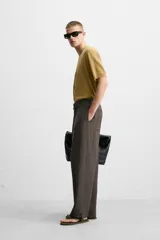 Pantalón marrón oscuro de corte amplio, con cintura ajustable con cordón, bolsillos plastrón delanteros y traseros, detalle de costuras frontales y cierre frontal con cremallera y gancho metálico oculto.