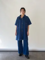 Vestido camisero corto de denim azul, con cuello camisero, mangas cortas y abotonadura frontal.