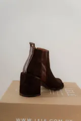 Botines de caña baja color marrón chocolate, confeccionados en gamuza con paneles laterales elásticos de cuero liso. Presentan puntera fina, cierre lateral con cremallera y tacón bloque.
