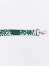 Llavero con cinta estampada con motivos de Mickey Mouse y la frase "Enjoy the now" en verde y blanco. Incluye gancho metálico plateado.