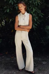 Pantalón de jean color crudo, de tiro alto y corte bootcut. Presenta cinturón fino del mismo tejido, bolsillos de parche en la parte trasera y cierre frontal con cremallera y botón.