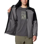 Campera tipo softshell con capucha, de color gris y negro. Presenta un diseño bicolor con el cuerpo principal gris y los hombros/mangas superiores en negro. Cuenta con cierre frontal de cremallera, bolsillos laterales con cremallera y puños elásticos.