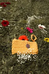 Bolso de mano tejido a crochet en trapillo grueso color borgoña, con asa corta y cierre con botón metálico plateado con logo.
