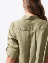 Camisa blanca de lyocell, marca Cyrus. Tiene cuello con solapa, abertura central con botones, mangas largas regulables con presilla y botón, y dos bolsillos delanteros aplicados.