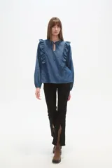 Blusa blanca de calce holgado con cuello en V y lazo frontal. Presenta detalles de volados en el pecho y cuello, y mangas largas con puños elásticos.