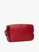 Cartera tipo cámara estructurada de color rojo, confeccionada en poliuretano. Presenta un cierre principal de cremallera y un monograma metálico TH en la parte delantera. Incluye una correa larga ajustable con detalles distintivos de la marca.