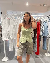 Chaleco de lino color verde claro, con escote en V y cierre frontal de botones. Presenta dos bolsillos de parche en la parte delantera inferior y un corte ligeramente peplum en el ruedo.