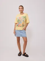 Remera amarilla de algodón con estampado de playa hawaiana con palmeras, flores y tabla de surf.