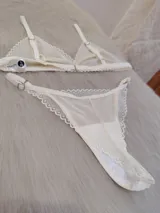 Conjunto de lencería color champagne, compuesto por un corpiño triangular de encaje con tirantes finos y una bombacha less de encaje con tiras ajustables.