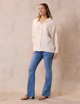 Camisa blanca de algodón con textura arrugada, cuello con solapa, abertura central con botones y bolsillo aplicado en el pecho. Mangas largas con largo regulable mediante presilla y botón.