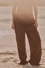 Pantalón marrón de tejido fluido, tiro medio, cintura elástica ajustable con cordones, bolsillos laterales y falsos bolsillos de vivo en la espalda.